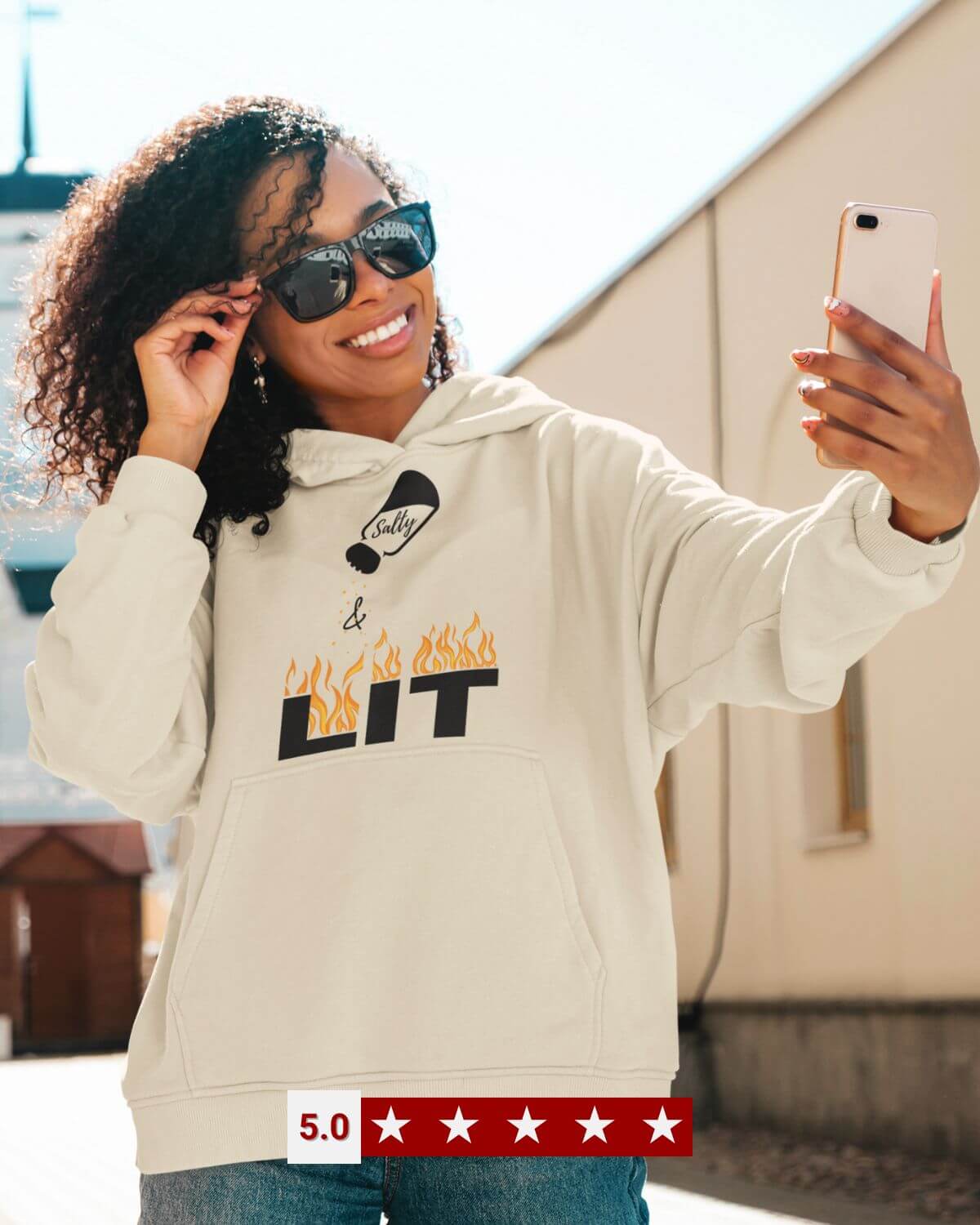 Smiling woman taking a selfie in the cream “Salty & Lit” faith hoodie by Giant Slayer, backed by a five-star customer score.